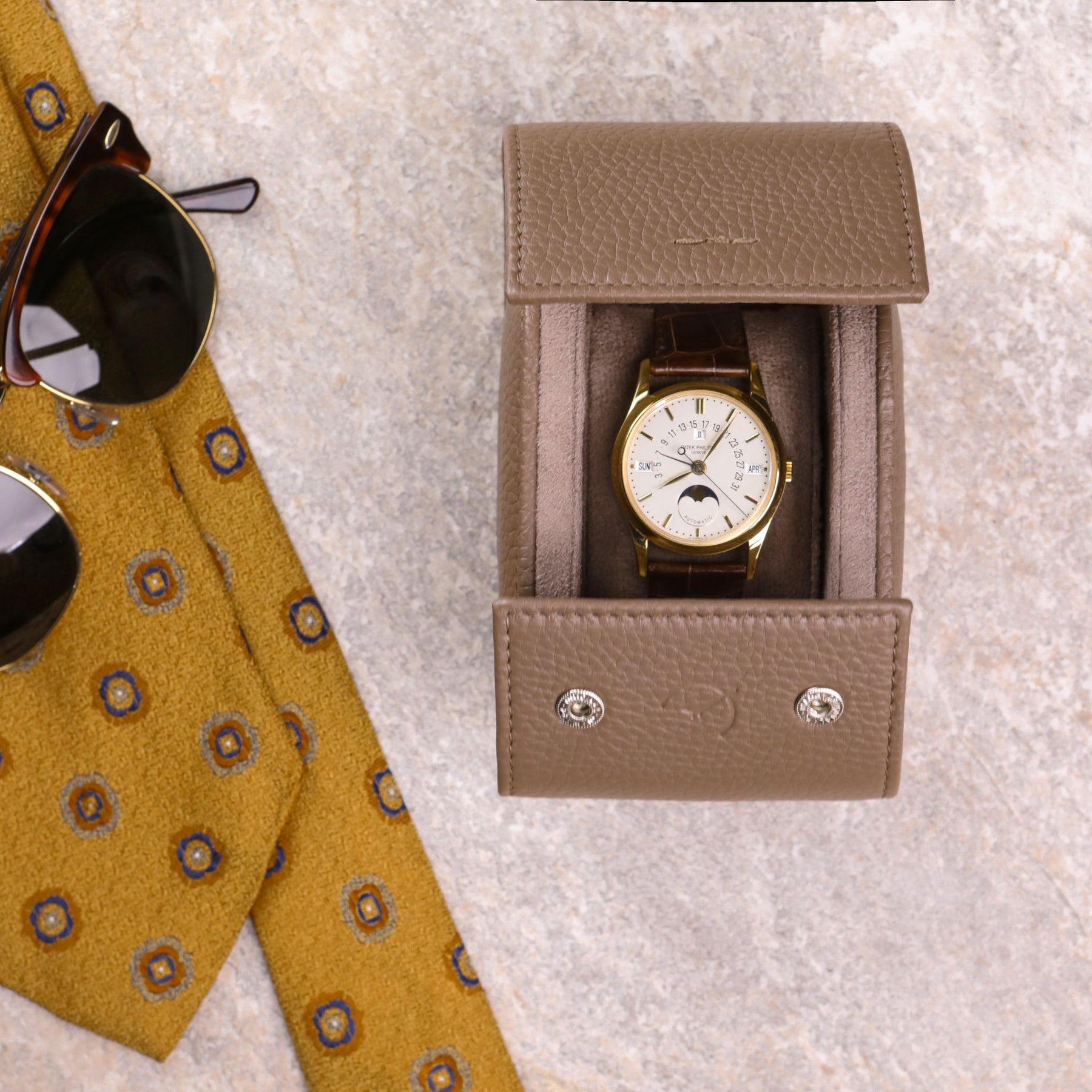 Rotolo porta orologio color tortora con Patek Philippe calendario al suo interno e occhiali vintage e cravatta sul lato sinistro