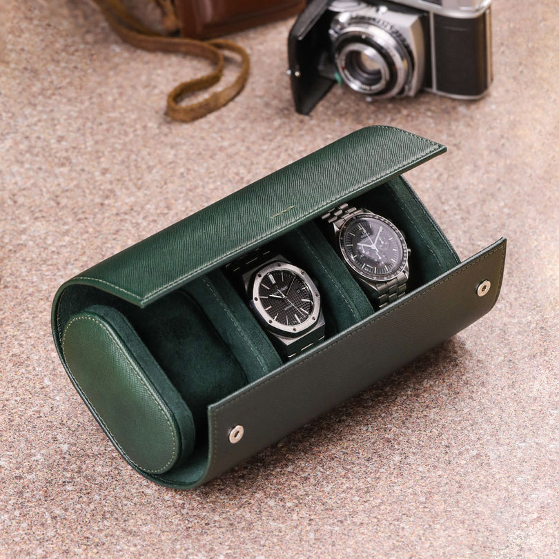 Rotolo porta orologi da 3 in pelle saffiano verde con Audemars Piguet Royal Oak e Omega Speedmaster Moonwatch all'interno e macchina fotografica vintage sullo sfondo